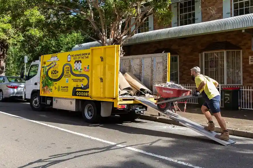 A man pushing a wheelbarrow to a goodbye junk yellow truck